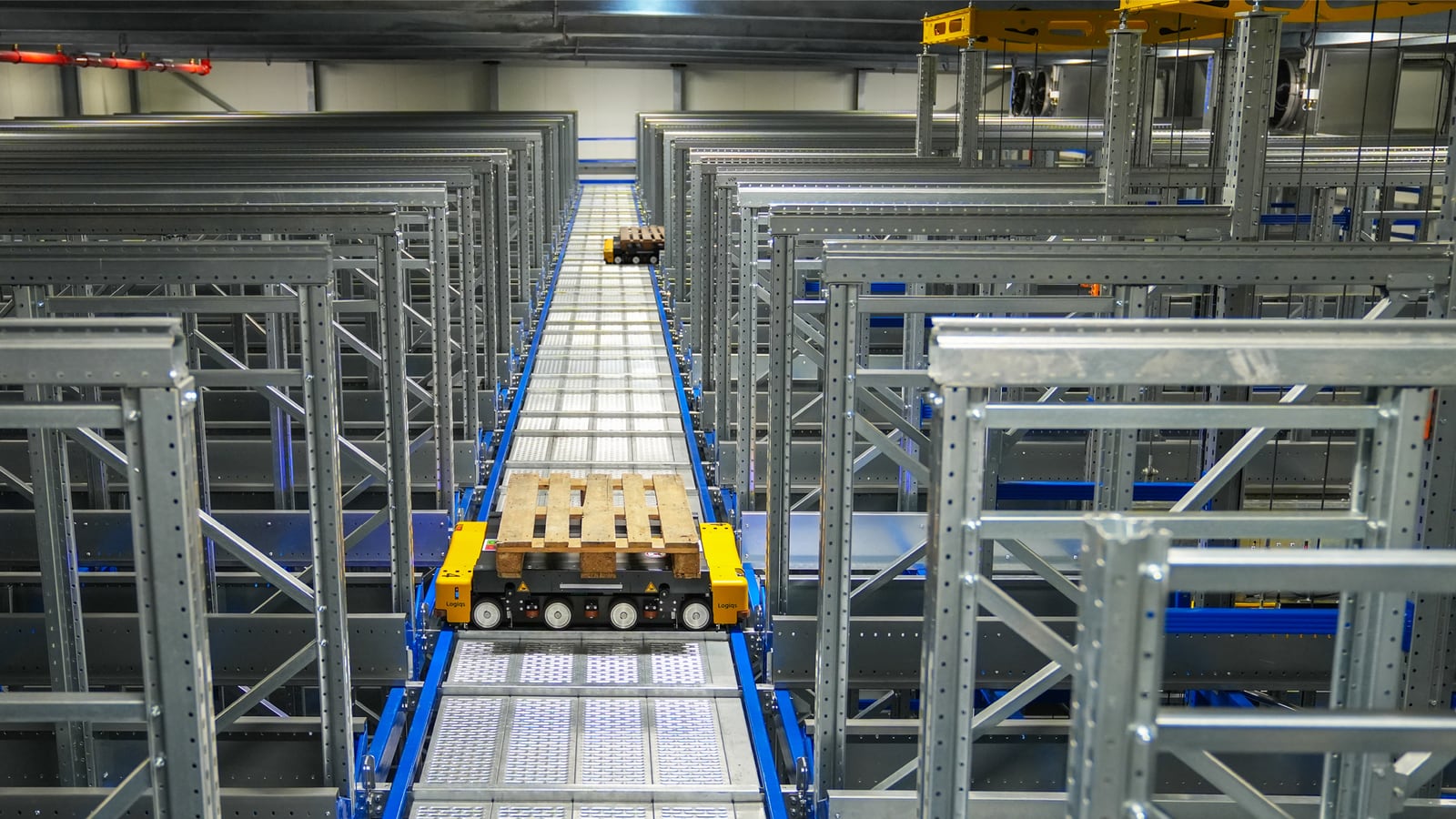 Automated pallet carrier moving through a high-rack warehouse.