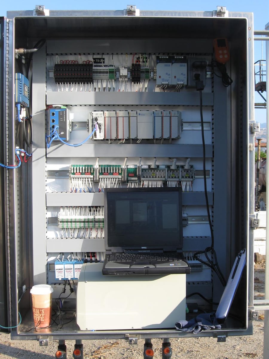 Industrial control cabinet containing a PLC, network switch, relays, wiring and a laptop