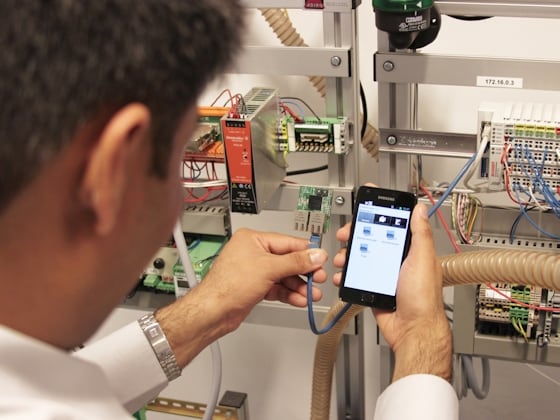 Engineer holding a mobile device beside an industrial control cabinet during OPC-UA system commissioning