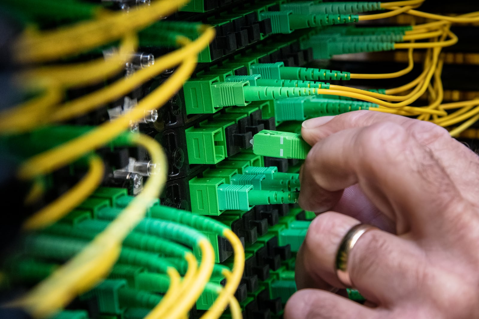 Technician connecting a green fiber-optic jumper cable in a data-center patch panel