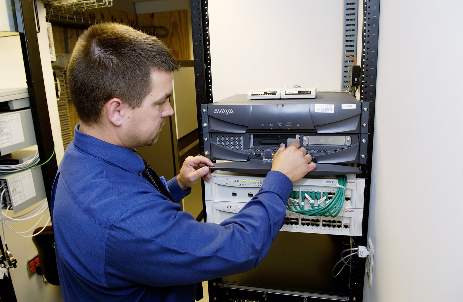 IT technician checking cables and controls on network equipment in a server rack