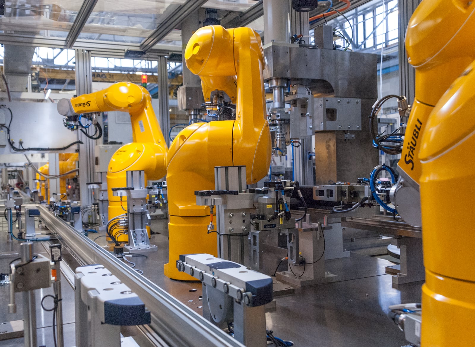 Yellow industrial robot arms operating beside fixtures and conveyors on an automated manufacturing line