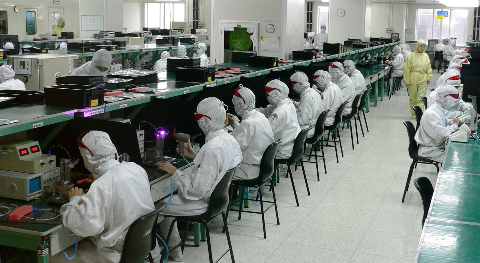 Electronics factory workers in protective clothing assembling and inspecting components along production benches