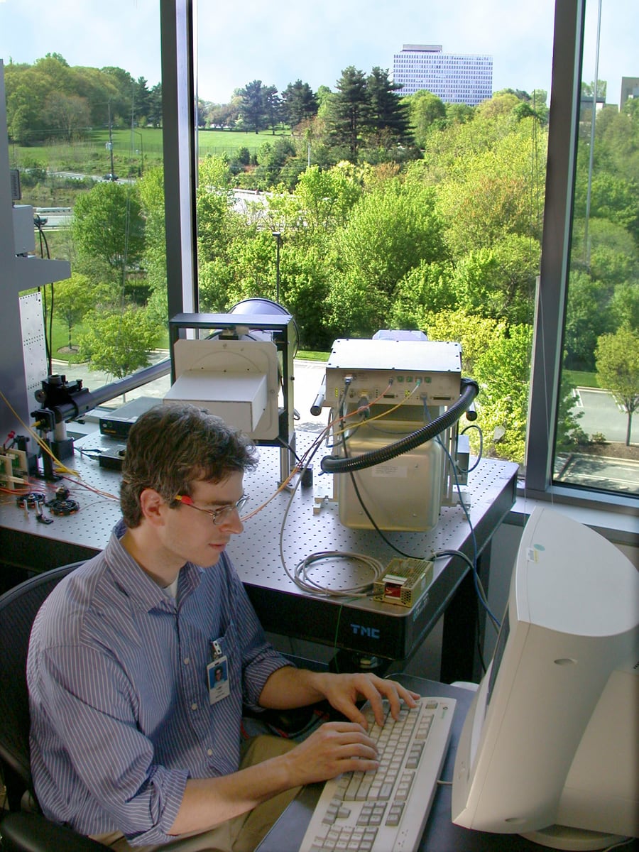 Physicist configuring a free-space quantum key distribution receiver beside a telescope and optical equipment