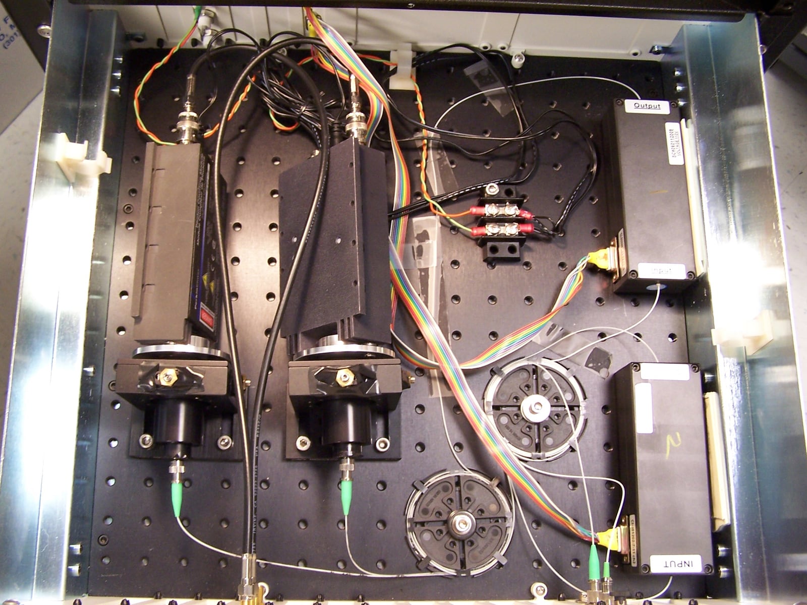 Top-down view of the detection stage of a prototype quantum key distribution system, with optical components, fibre leads, cables, and labelled input and output paths.