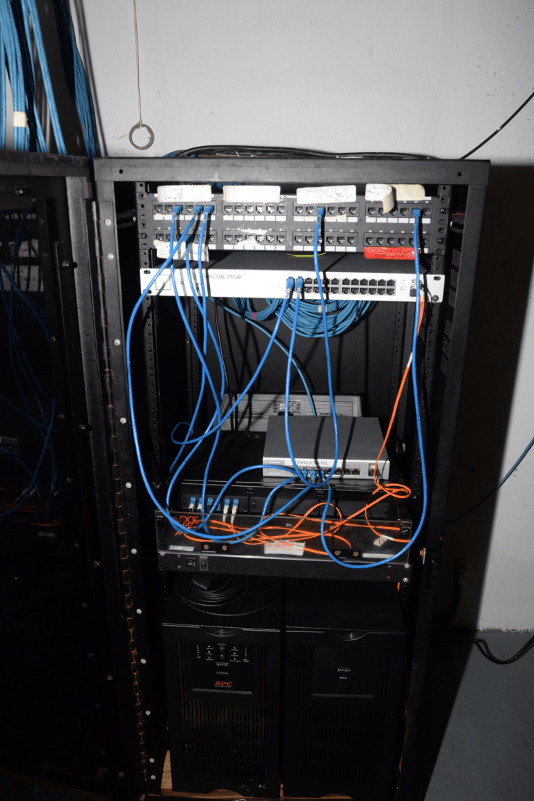 EFTA00002005 Server rack filled with networking equipment and cables including blue Ethernet connections and orange wires in a data center environment for cloud infrastructure, DevOps and platform engineering