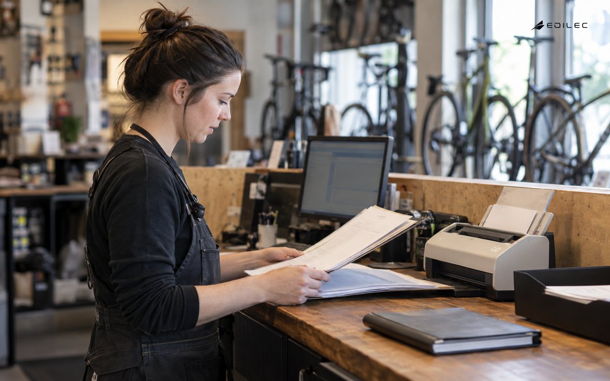 A workshop employee inspects a paper service folder beside document-processing equipment.