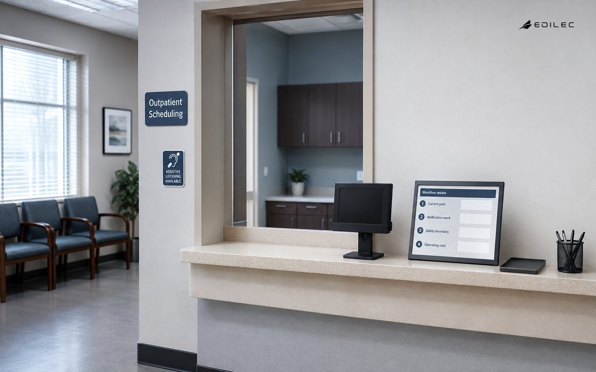 Wide view of empty outpatient scheduling office with accessible reception window, orderly forms and small ordinary opaque monitor on a stand.