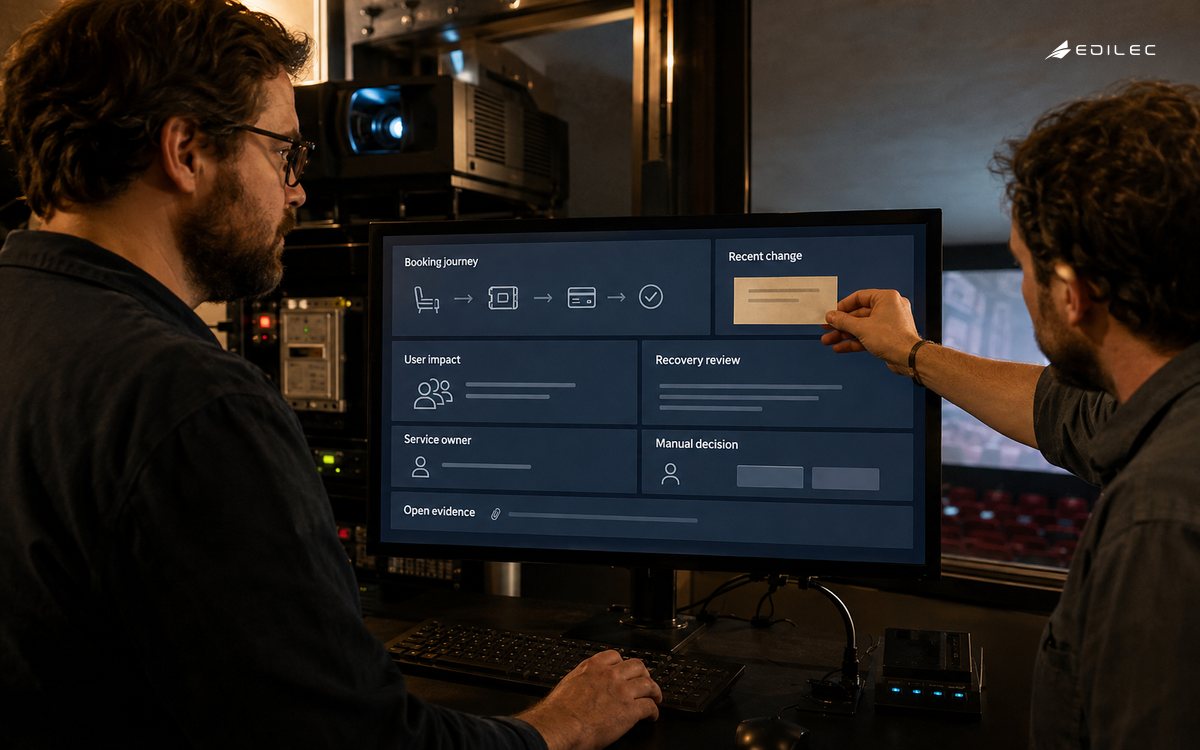 A cinema operations lead reviews a supported monitor while a colleague places a recent-change note beside a booking journey card.