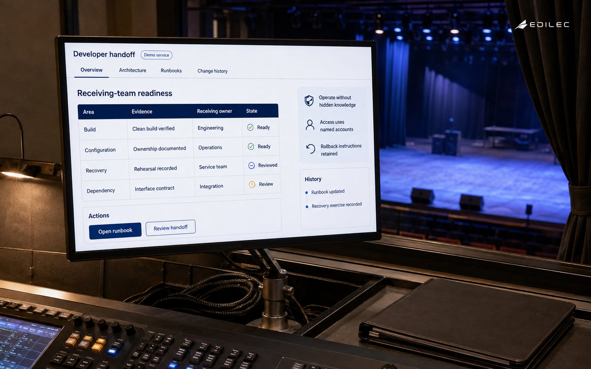 Theatre lighting software maintenance corner overlooking an empty rehearsal stage through a window. The manufactured display shows developer handoff in a fictional demonstration.