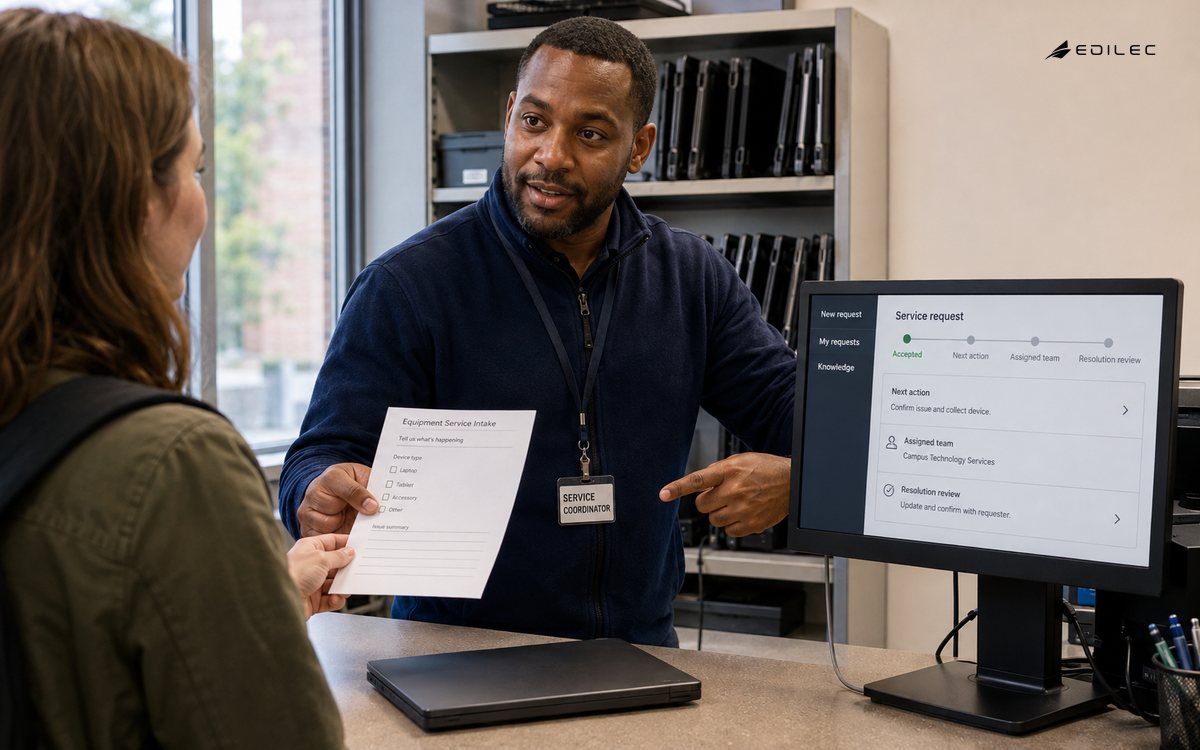 A service coordinator standing behind the counter accepts a paper equipment-service intake sheet and points toward a small opaque LCD monitor on a commercial stand.