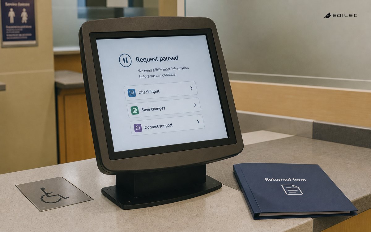 Medium documentary photo of a public service kiosk area, ordinary opaque touchscreen in mounted housing on accessible counter with returned form folder beside it.